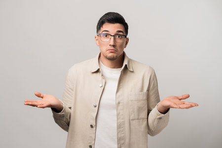No clue. A man in a beige overshirt and eyeglasses raising his palms and shrugging his shoulders in confusion. A perfect mix of uncertainty and casual charmの写真素材