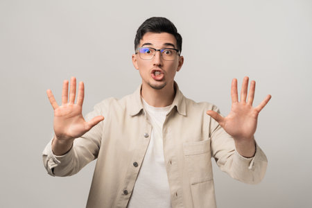 Stop. Calm down. A reassuring man in eyeglasses and a beige overshirt holding his hands up with open palms, gesturing for peaceの写真素材