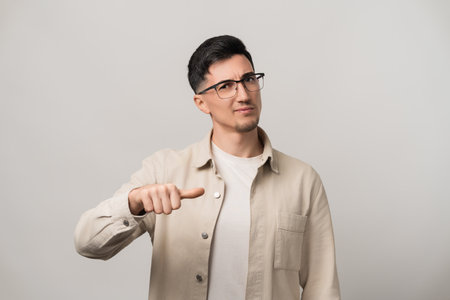 Lost in decision. An uncertain man with eyeglasses holding a deciding thumb, deep in thought with a doubtful expression. Classic gesture meets modern indecisionの写真素材