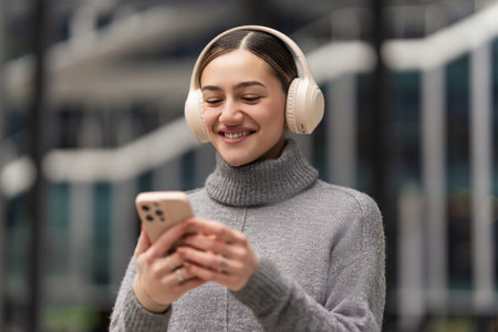 Scrolling, sharing, staying connected. A woman with headphones and smartphone reacts to social media updates, capturing real-time engagement in a world driven by digital connectionsの写真素材