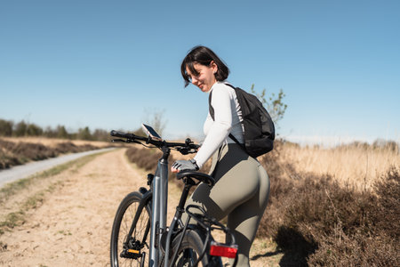 Free-spirited woman with backpack jumps on her bike in the great outdoors, capturing the essence of adventure and healthy livingの写真素材