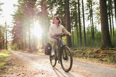 Wellness in motion, a vibrant woman pedals her way through a peaceful forest retreat at sunsetの写真素材