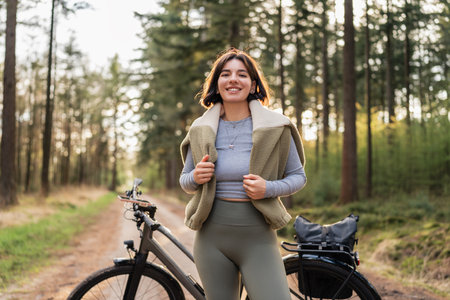 Young woman biking under tall trees, linking mindful movement, seasonal escape, and sport-infused travelの写真素材