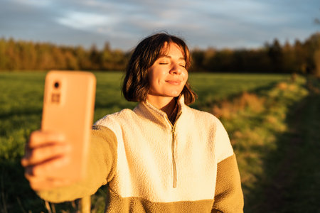 Young woman enjoying golden hour in nature, blending influencer lifestyle with outdoor well-being and digital mindfulnessの写真素材