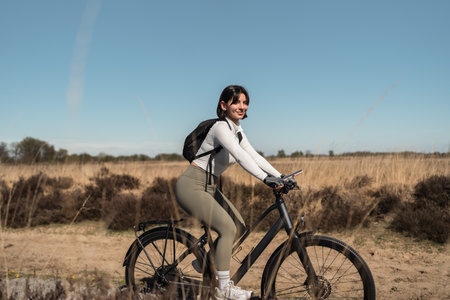 Female cyclist rides a sandy coastal trail, merging summer holiday joy with sport, travel freedom, and mindful well-beingの写真素材