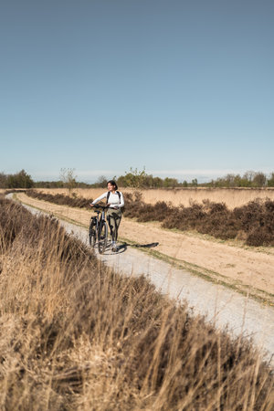 Multiracial woman with short hair walks her bicycle along a quiet nature trail, blending eco-friendly lifestyle, relaxation, and personal wellnessの写真素材