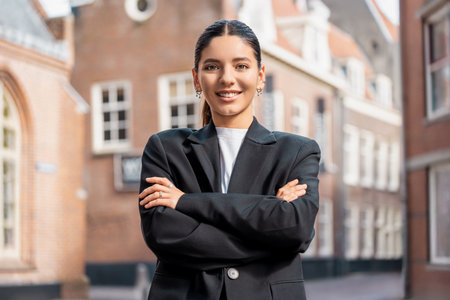Attractive young woman realtor in sleek black suit stands confidently on city street, ideal for real estate branding, urban professionalism, career empowerment, or modern leadershipの写真素材