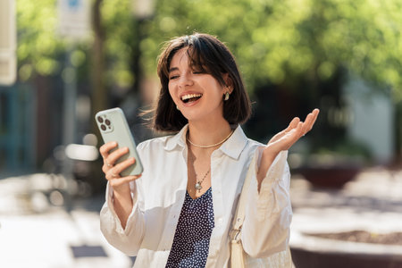 City pulse. Latina woman with a beautiful smile and short hair uses banking app while waiting at the bus stop in a white casualの写真素材