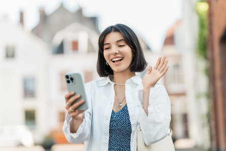Face time. Latina woman with short hair and a casual white shirt chats with loved ones while handling banking tasks on mobileの写真素材