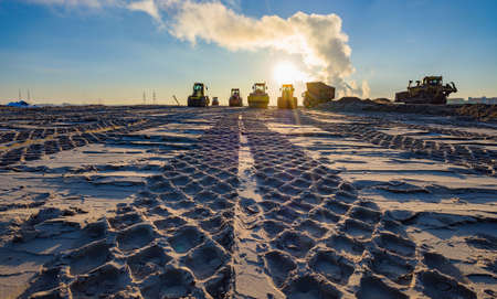 roller compacts soil in embankment on the road's construction. sand consolidation on road-building. Compactor driving on sandy. wheel marks on the sand. hard work. transportation of sand by trucksの写真素材