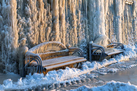 Park bench is covered with ice. the wall of ice and icicles. unusual natural phenomenonの写真素材
