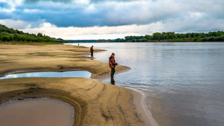fishermen catch pike on spinning. man fishing on the river with a sandy beachの写真素材