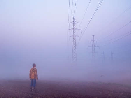 transmission towers and man in the fog at the background of the dawn sky. High Voltage power line silhouette during the sunset in a clear skyの写真素材