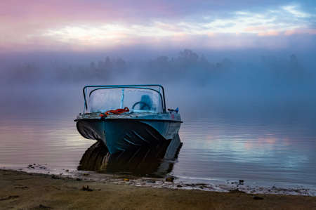 boat on the banks of the foggy river at dawn. beautiful mystical landscape with river and boatの写真素材