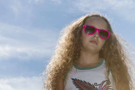 Young girl in sunglasses fixing her long blond hair in the sunlight on a hot afternoon.の写真素材