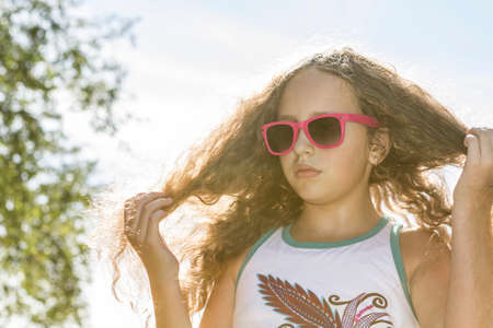 Young girl in sunglasses fixing her long blond hair in the sunlight on a hot afternoon.の写真素材