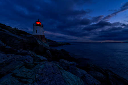 Lighthouse on a rocky shore at sunset.