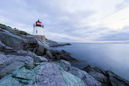 Lighthouse on a rocky shore at sunset.の写真素材