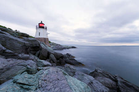 Lighthouse on a rocky shore at sunset.の写真素材