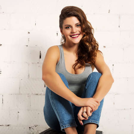 Lovely girl in jeans and top sitting and smiling. White brick wall not isolatedの写真素材