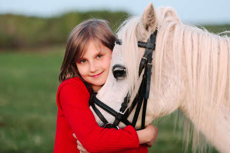 Little young girl in a red dress hugging his head a white horse Outdoorsの写真素材