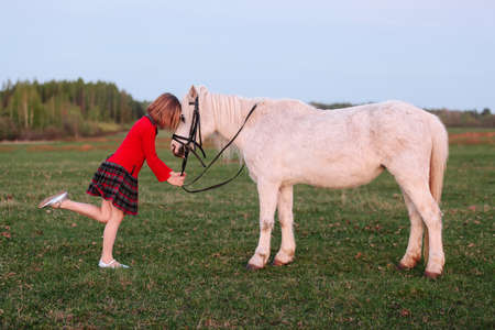 Small model of a young girl put her child in a small white pony Outdoorsの写真素材