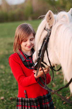 Small model of a young girl child looks at a white horse Outdoorsの写真素材