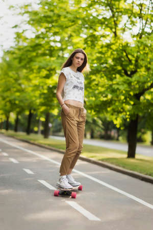 Young girl student model pants shirt and sneakers rides on the bike path in the park and looks into...