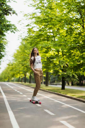 Beautiful young girl hipster T-shirt, shorts and sneakers rides on the track in park on a longboard. Skateboarding. Outdoors, lifestyleの写真素材