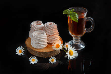 handmade white marshmallows with daisies and a cup of tea on a black backgroundの写真素材