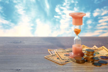 Time is money. Financial concept of money with a clock and coins of different countries. Hourglass.の写真素材