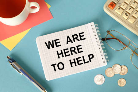 We are here to help, is written on a notepad, on an office desk with office accessories.