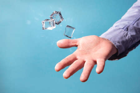Male hand throws ice cubes. Ice cubes on a blue background.の写真素材