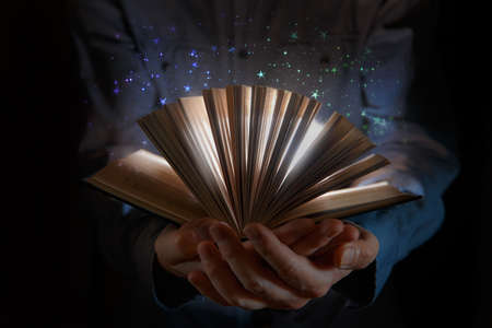 The human hand holds a magic book with magic lights against a dark background