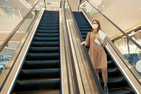 Business woman in a protective mask with a computer on the background of a modern corporate...
