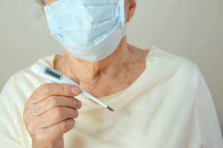 An elderly woman in glasses puts on a medical mask on her face. Elderly woman in glasses with a...