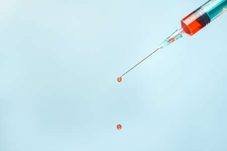 Syringe with a drop of blood at the end of the needle on a blue background. Medical procedures
