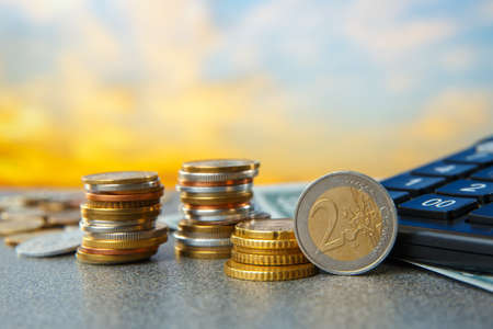 Coins in heaps and a calculator on a sunrise background. High cost concept.の写真素材