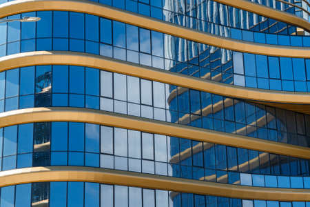 Part of a super modern business building against the blue sky. Sky and clouds are reflected in the windows.の写真素材