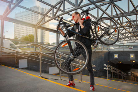 A young biker climbs the stairs of the underpass and carries a bicycle on his shoulder.
