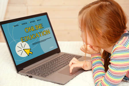 Little girl looks at the computer. ONLINE EDUCATION is written on the computer monitor.の写真素材