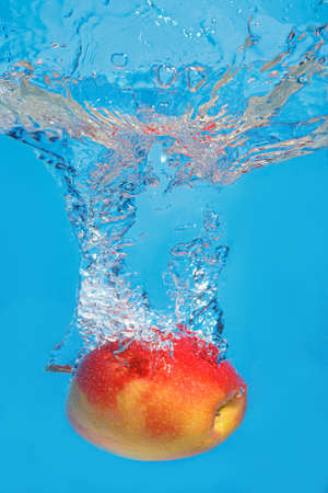 Fresh apple drops in water with splash on a blue backgroundの写真素材