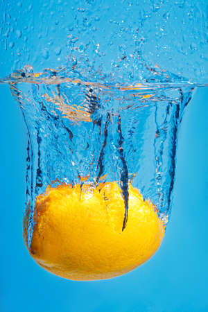 Fresh lemon drops in water with a splash on a blue background