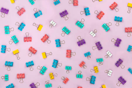Multi-colored binder clips scattered over a pink background. Creative background.の写真素材
