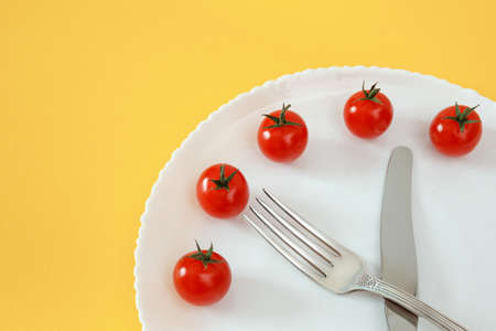 Cherry tomatoes clock on plate with cutlery. Diet food