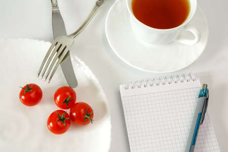 Cherry tomatoes on a plate with cutlery and a cup with tea. Notebook for recording and counting...