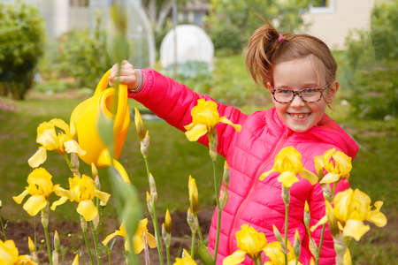 A girl in a bright pink jacket is watering flowers in the gardenの写真素材