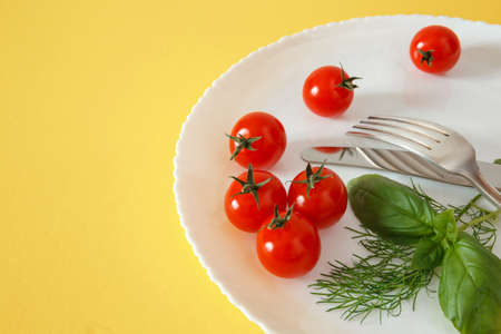 Cherry tomatoes on a plate with basil and cutlery. Diet food