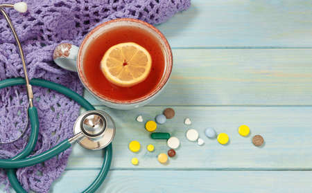 Hot tea, pills, knitted scarf and stethoscope. Cold season.の写真素材