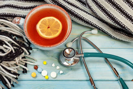Hot tea, pills, knitted scarf and stethoscope. Cold season.の写真素材